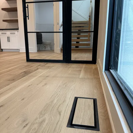 Modern interior with light wood flooring, black-framed glass door, stairs, and kitchen area in background