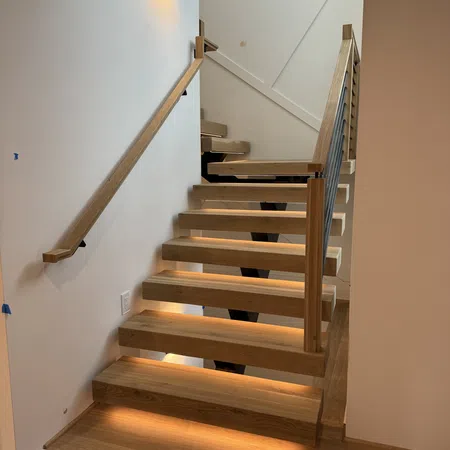 Modern wooden staircase with under-step lighting and minimalist handrails in a bright interior.