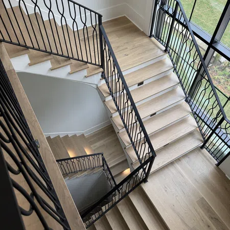 Modern wooden staircase with black metal railings inside a bright room with large windows