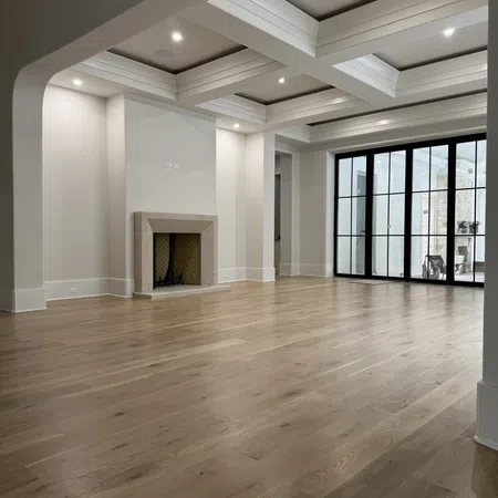 Spacious empty living room with hardwood floors, white walls, coffered ceiling, fireplace, and large glass doors.