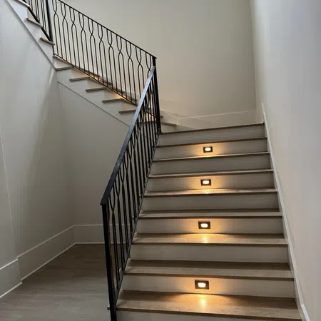 Modern indoor staircase with wooden steps, black metal railing, and built-in step lights in a bright space.
