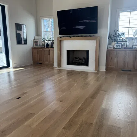 Bright living room with light wood flooring, fireplace, mounted TV, wooden cabinets, and natural light from windows.