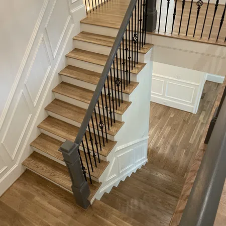 Interior wooden staircase with black metal balusters and white paneled walls in a modern home.
