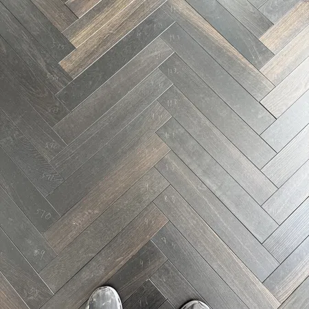 Top view of black and brown herringbone wood flooring with chalk markings and worn gray shoes.