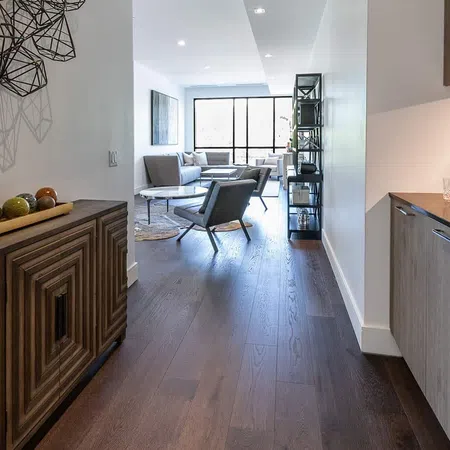 Modern living room with dark hardwood floors, gray chairs, wooden cabinets, and geometric wall art.