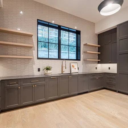Modern kitchen with gray cabinets, light wood flooring, open shelves, and a large window with natural light.