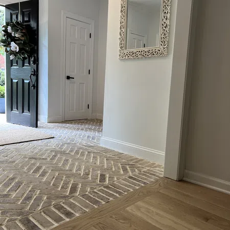 Entryway with open black door, decorative wreath, herringbone brick flooring, white walls, and ornate wall mirror.