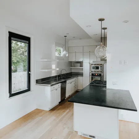 Bright modern kitchen with white cabinets, black countertops, wooden floor, and pendant lights over island.