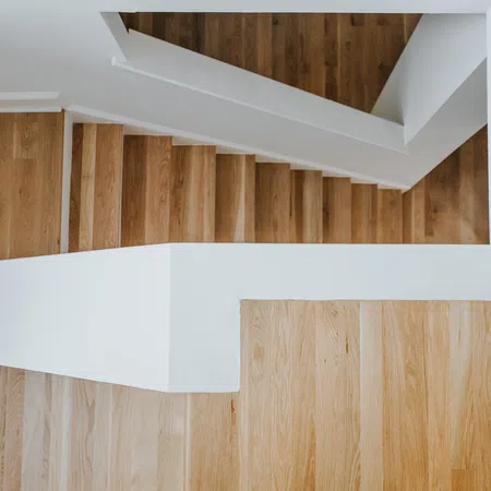 Top view of a modern wooden staircase with white railings in a minimalist interior space.