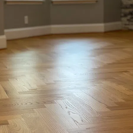 Close-up of smooth, polished hardwood floor with herringbone pattern in a bright room.