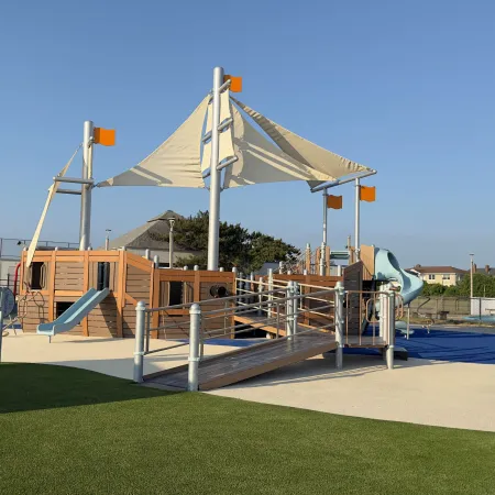Bright and inviting playground with slides, a shaded area, and green grass under a clear blue sky.