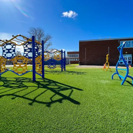Colorful playground equipment on green artificial turf under a clear blue sky.