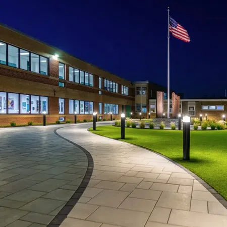 Modern school courtyard at night with illuminated walkway, green lawn, and US flag on flagpole.