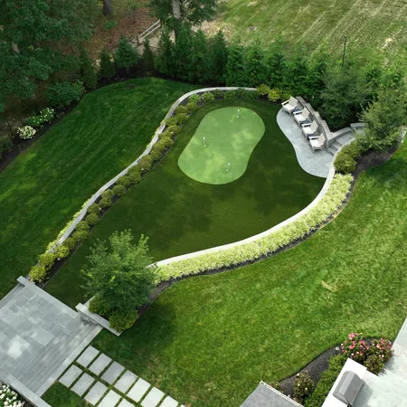 Aerial view of a manicured backyard with a putting green, seating area, and surrounding lush landscaping.