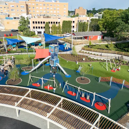 A colorful playground with slides, swings, climbing nets, shaded areas, and children playing on the equipment under a sunny sky.