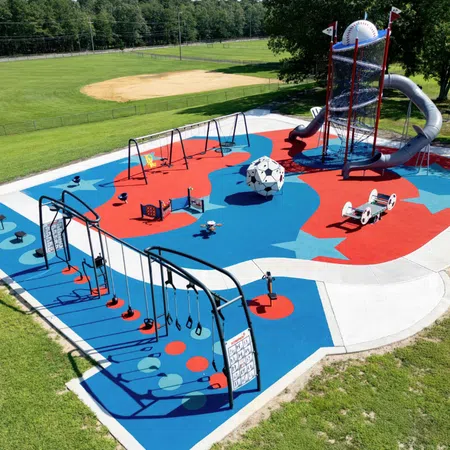 Colorful outdoor playground with swings, slides, climbing structures, and a soccer ball centerpiece on blue and red surface.