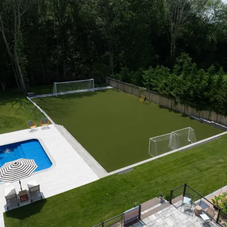 Backyard with a swimming pool, patio seating, basketball hoop, and an artificial turf soccer field with goals.