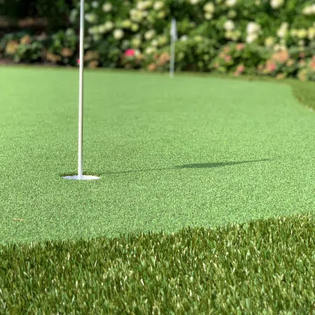 Close-up of golf ball near hole on artificial putting green with vibrant grass and garden background