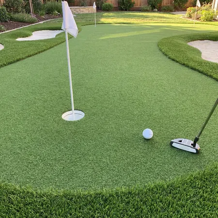 Close-up of a golf ball near the hole on a backyard putting green with a putter and sand bunkers.