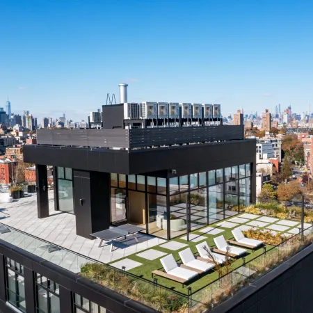 Modern rooftop terrace with lounge chairs, glass walls, and city skyline under a clear blue sky.