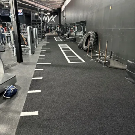 Interior view of a modern gym with workout machines, large tires, mirrors, and marked training area on black flooring.