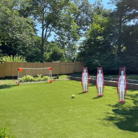Backyard soccer practice setup with goal, three mannequin defenders, and soccer ball on green grass.