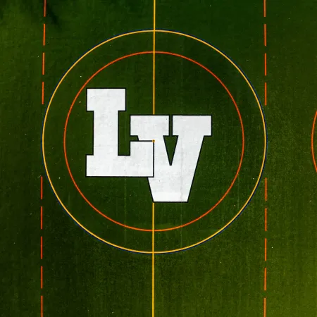Aerial view of a sports field with green turf and white letters LV in the center circle surrounded by colored lines.