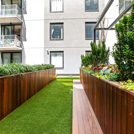 Modern apartment building courtyard with green artificial grass and elevated wooden planter boxes filled with plants.