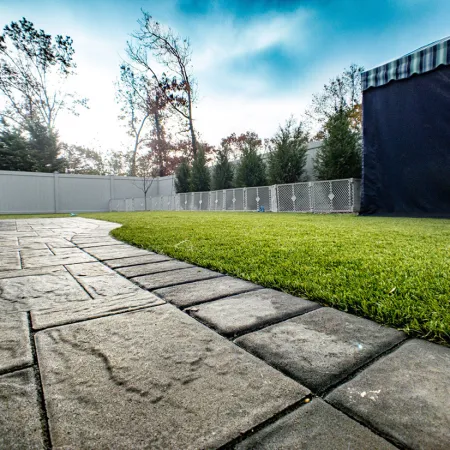 a concrete walkway with grass and a fence and trees