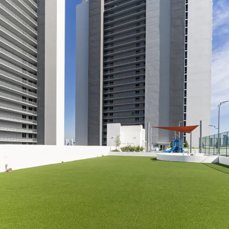 Modern rooftop playground with artificial grass between tall residential buildings under clear sky.