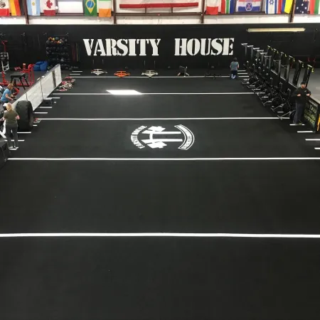 Wide view of Varsity House gym with black flooring, workout equipment, weightlifting area, and international flags overhead