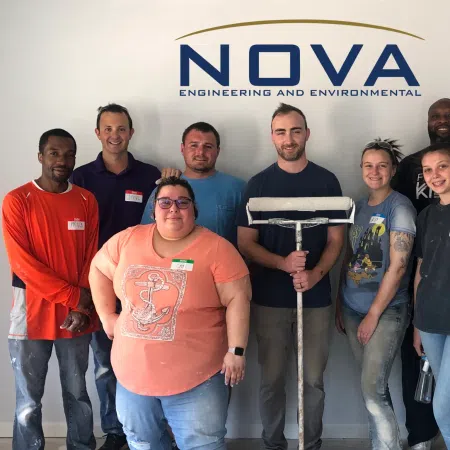 Group of diverse NOVA Engineering team members posing in front of company logo wearing casual work attire