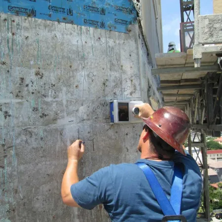 Construction worker in hard hat using device to scan wall on a building site with scaffolding nearby