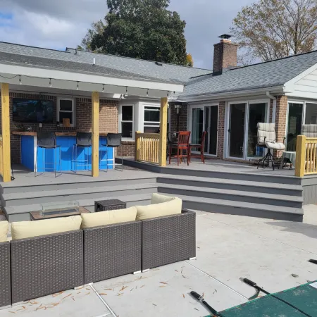 Modern backyard patio featuring a covered bar area, outdoor seating, and a multi-level deck attached to a brick house.