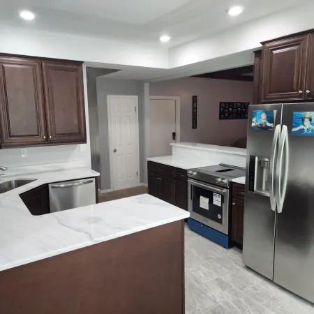 Modern kitchen with dark wood cabinets, white marble countertops, stainless steel appliances, and recessed lighting.