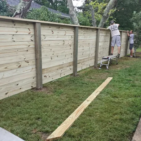 Two men installing a new wooden privacy fence in a backyard with green grass and trees.