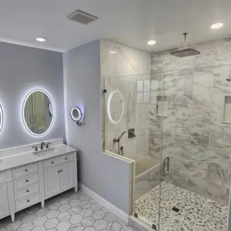 Modern bathroom with double white vanity, illuminated round mirrors, and glass-enclosed rain shower with marble accents