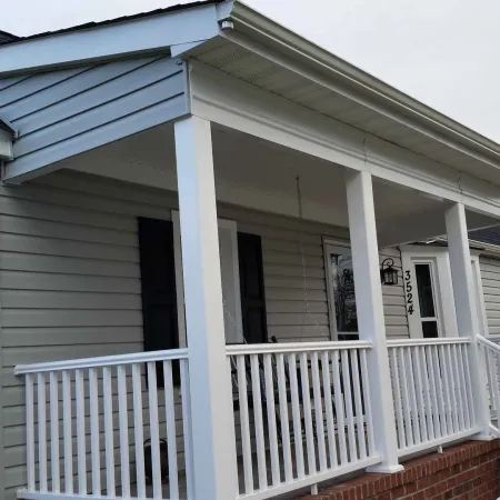 Front porch of a light gray house with white railings and brick steps under an overcast sky