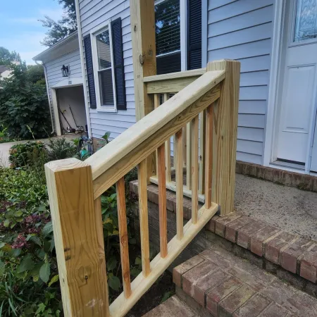 New wooden handrail installed next to brick steps at house entrance with white siding and black shutters.