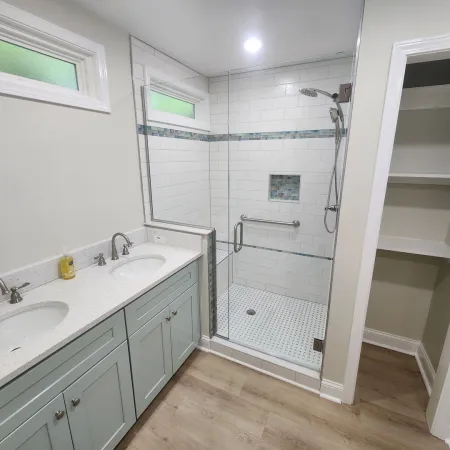 Modern bathroom with double vanity sinks, glass shower enclosure, light blue cabinets, and open shelving closet.