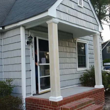 Small house entrance with brick steps, two columns supporting porch roof, and gray siding exterior