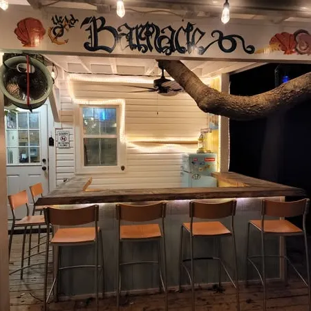 Cozy outdoor bar area with wooden counter, high stools, string lights, and a tree branch overhead at night