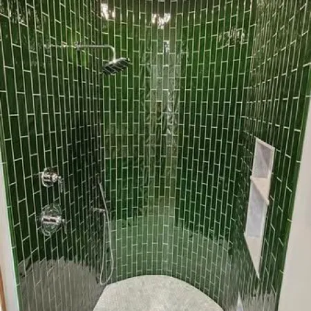 Curved shower with glossy dark green subway tiles and small white hexagonal floor tiles under ceiling light.