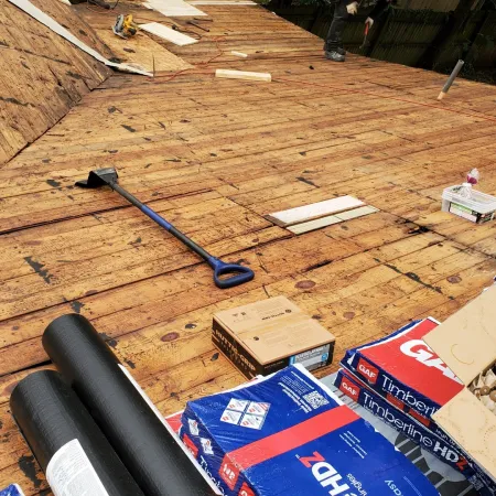 Roof decking stripped and prepared for new roofing with tools and materials laid out on wooden boards.