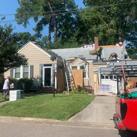 Workers repairing and replacing the roof of a beige suburban house with ladders and materials outside.