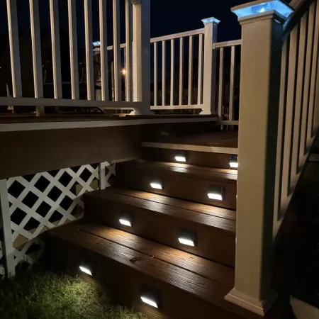 Outdoor wooden stairs with white railings illuminated by small modern LED lights at night.
