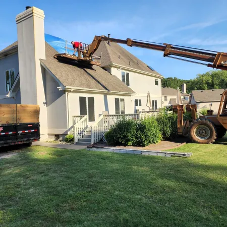 Construction worker on a lift repairing a residential roof with debris trailer nearby on sunny day
