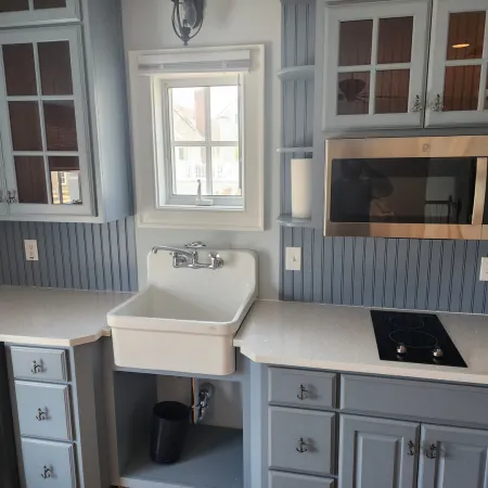 Modern kitchen with blue cabinetry, white farmhouse sink, stainless steel microwave, and electric stovetop under window.