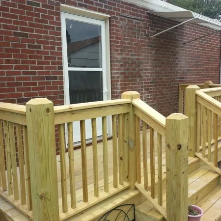 Newly built wooden front porch and stairs attached to a brick house exterior with a white door.