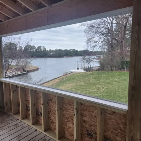 View from a wooden porch under construction overlooking a grassy yard and lake with docks and trees on a cloudy day